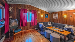 A cozy cabin-style room with wooden walls, a gray sofa, a wooden coffee table, and a chair.