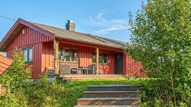 A red wooden cabin with a porch, steps leading up to the entrance, and a chimney.