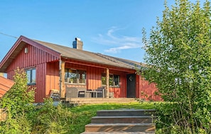 A red wooden cabin with a porch, steps leading up to the entrance, and a chimney.