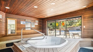 Un área de spa con un jacuzzi, paredes de madera y un ventanal que da a una zona de estar exterior.