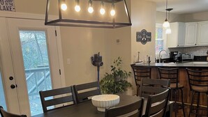 Un comedor con una mesa y sillas de madera oscura, una lámpara colgante y vista a la cocina al fondo.