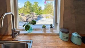 Eine Küche mit Spüle, einem Fenster mit Topfpflanzen und Blick auf Gartenmöbel.