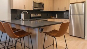 Une cuisine moderne avec des meubles en bois, un réfrigérateur en acier inoxydable, un four à micro-ondes et un îlot central doté de tabourets de bar.