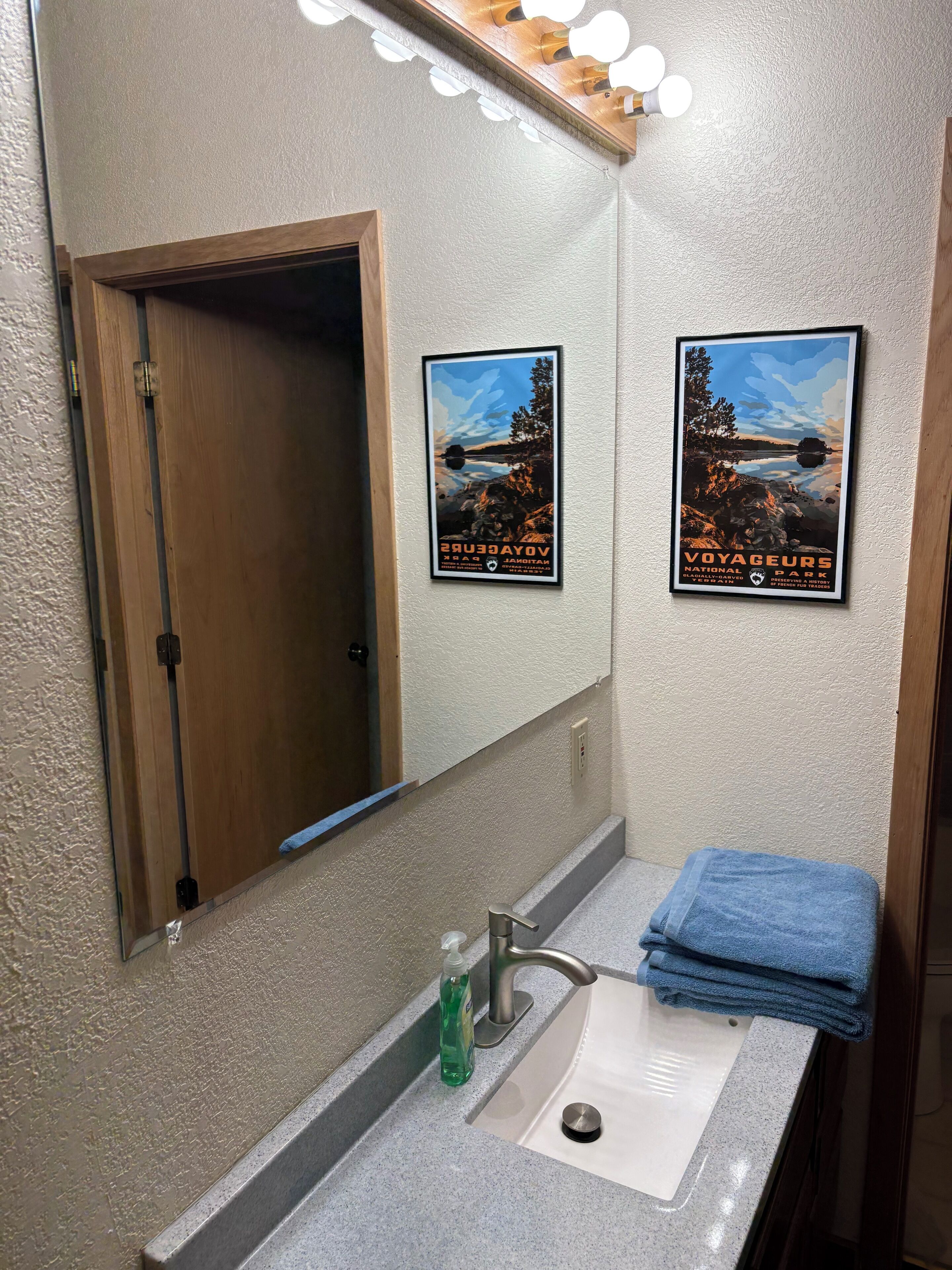 Un baño con lavamanos, espejo y dos carteles enmarcados en la pared.