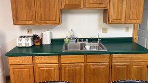 Una cocina con armarios de madera, encimera verde, tostadora, fregadero y un bloque de cuchillos.