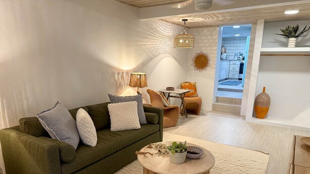 Ein modernes Wohnzimmer mit einem grünen Sofa, einem runden Couchtisch und einem Essbereich mit Korbstühlen.