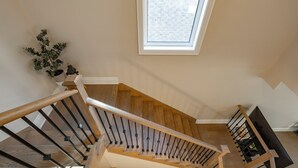 A wooden staircase with a skylight, a potted plant, and a bookshelf.