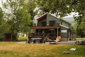 Een chalet van twee verdiepingen met een balkon, buitenmeubels en een hangmat.