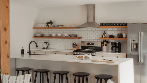 Une cuisine moderne avec des carreaux blancs, des étagères en bois, une cuisinière en acier inoxydable et un réfrigérateur encastré.
