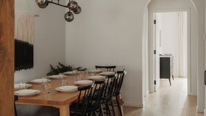 Un coin repas avec une table et des chaises en bois, un luminaire suspendu et un couloir menant à une autre pièce.