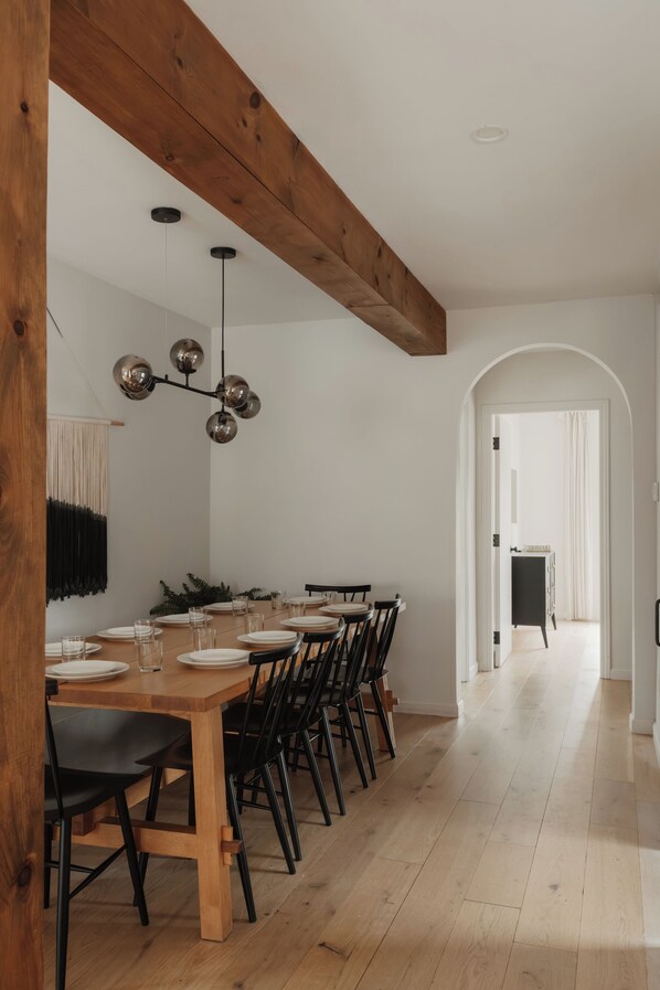 Un comedor con una mesa y sillas de madera, una lámpara colgante y un pasillo que conduce a otra habitación.