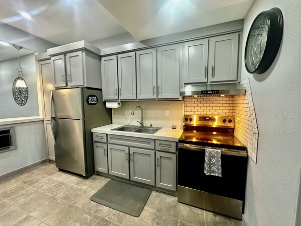 Una cocina moderna con gabinetes grises, electrodomésticos de acero inoxidable, un horno negro y un salpicadero de azulejos.