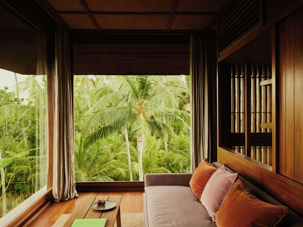 A room with a wooden ceiling, a large window with curtains, a sofa with cushions, and a small table with a decorative item.