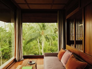 A room with a wooden ceiling, a large window with curtains, a sofa with cushions, and a small table with a decorative item.
