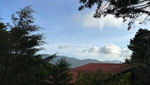 A mountainous landscape with a red-roofed building partially obscured by trees. - Secluded Chalet in Cerro de la Muerte Coffee Region with Fireplace & Green Views (San José)