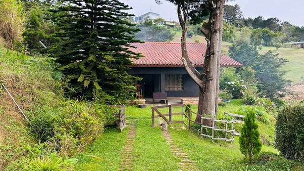 A small house with a red roof, surrounded by lush greenery and a wooden fence. - Secluded Chalet in Cerro de la Muerte Coffee Region with Fireplace & Green Views (San José)