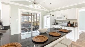 A modern kitchen with a central island, white cabinetry, a microwave, and a refrigerator. - Five minute walk to the beach, and a pool in Oak Island! Time for family fun! (Oak Island)