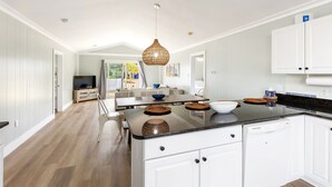 A modern kitchen with white cabinetry, a central island, and a dining area with a table and chairs. - Five minute walk to the beach, and a pool in Oak Island! Time for family fun! (Oak Island)