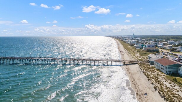 A coastal view with a pier extending into the ocean, beachfront properties, and a clear sky. - Five minute walk to the beach, and a pool in Oak Island! Time for family fun! (Oak Island)