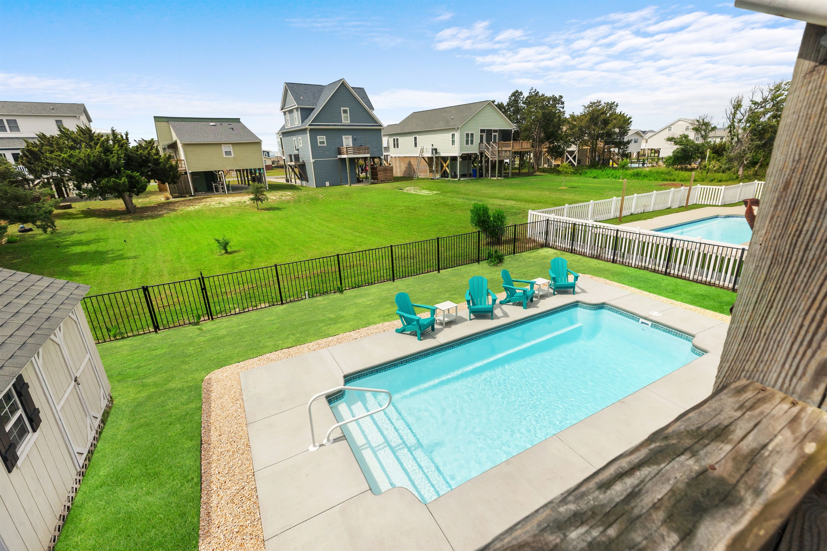 A residential backyard with a swimming pool, a wooden deck, and a fenced area.