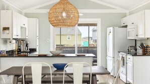 A modern kitchen with white cabinets, a central island, a hanging light fixture, and a view to the outside. - Five minute walk to the beach, and a pool in Oak Island! Time for family fun! (Oak Island)