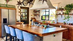 Een keuken met een centraal eiland, barstoelen, hangende sterlampjes en een bord met de tekst 'FRESH PRODUCE'.