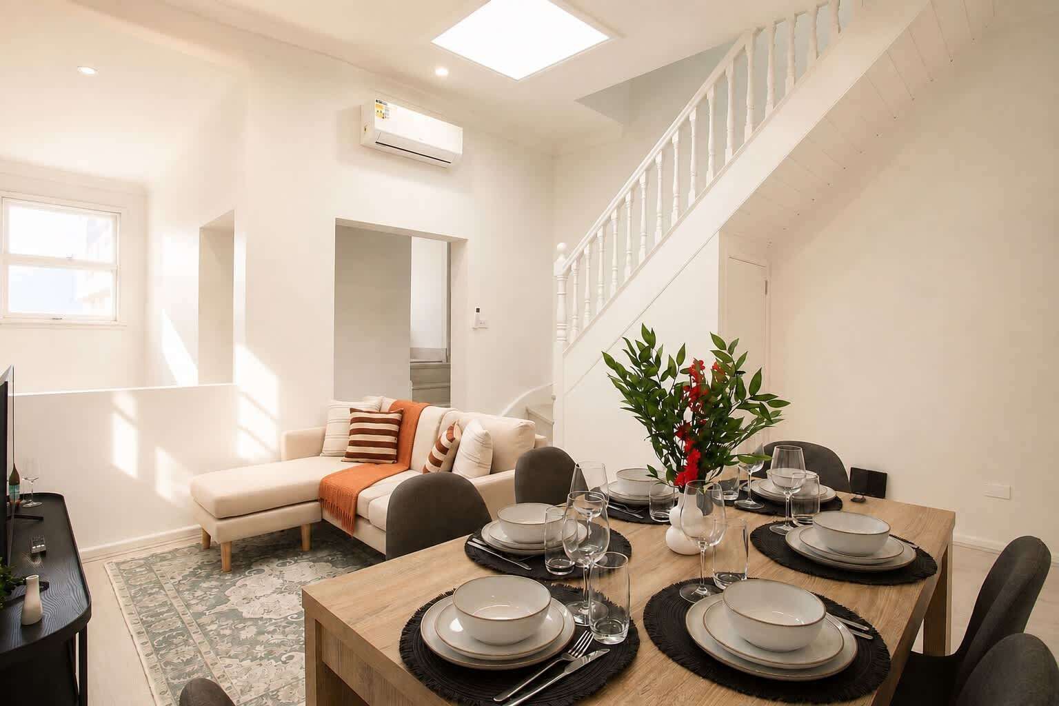 A modern living room with a dining area, a staircase, and a view of the outdoors.