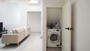 Un soggiorno moderno con un divano, una lavatrice e una porta che dà su un'altra stanza.