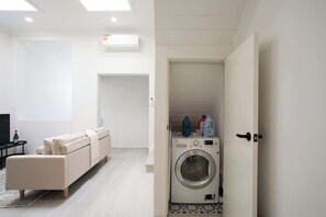 Una sala de estar moderna con sofá, lavadora y una puerta que da a otra habitación.