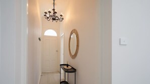 Un corridoio con un lampadario, uno specchio, un tavolo consolle con una pianta e una porta alla fine.