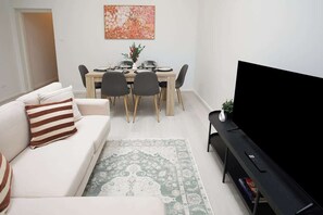 Un salon comprenant un canapé, une table à manger, des chaises, un téléviseur et un tapis.