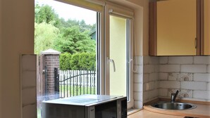 A compact kitchen with a microwave, a sink, and a view of a green garden through a sliding glass door. - 1 bedroom amazing apartment in Rowy (Rowy)