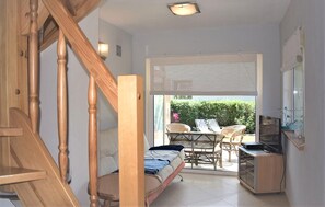 Une petite chambre comprenant un lit, une télévision, une petite table et une chaise. Une fenêtre offre une vue sur la verdure environnante.