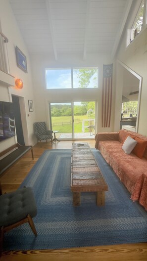 Ein geräumiges Wohnzimmer mit großem Fenster, einem Holztisch, einer Couch und einem gemusterten Teppich.