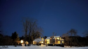 A snow-covered landscape with two houses illuminated by warm lights against a night sky. - Take 25-27% off the listed price 2026, 6 en-suite, pets, privacy, linens, ADA. (Provincetown)