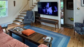 Amplia sala de estar con un televisor grande, escalera de madera y un rincón de asientos acogedor.