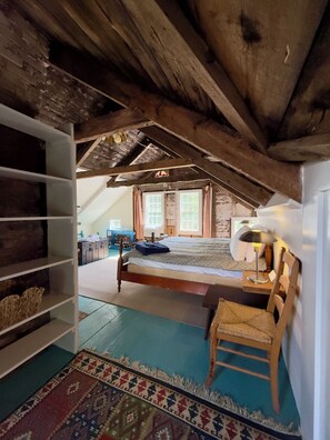 A room with a loft bed, wooden beams, a small chair, and a colorful rug. - 1800 Farmhouse · 6 Suites · Pets · Guest Cottage (Provincetown)