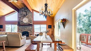 Un salón amplio con chimenea de piedra, techo de madera y grandes ventanales con vistas al exterior.