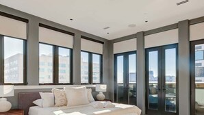 Een moderne slaapkamer met een groot bed, een bankje en uitzicht op de stad door ramen van vloer tot plafond.