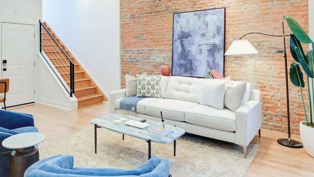 Ein modernes Wohnzimmer mit einem weißen Sofa, blauen Sesseln, einem Couchtisch und einer Ziegelwand als Blickfang.