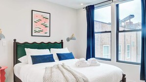 Ein Schlafzimmer mit einem Bett, einem Vorhangfenster, einer Wandlampe und einem gerahmten Bild.