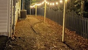 Un chemin menant à un bâtiment blanc, entouré d’une clôture en bois et illuminé de guirlandes lumineuses.