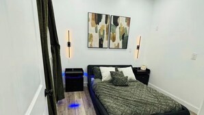 Une chambre à coucher comprenant un lit, une table de chevet, une lampe fixée au mur et des œuvres d’art abstraites.