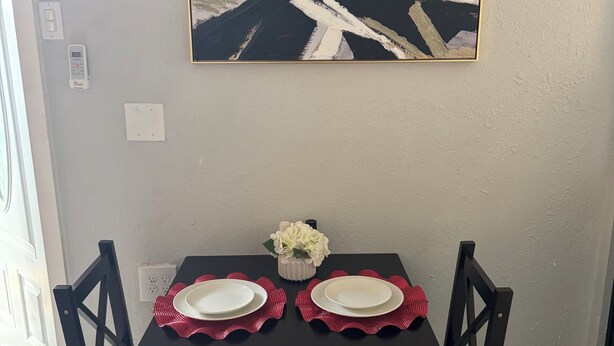 Una mesa de comedor con dos sillas, un florero con flores y un cuadro en la pared.