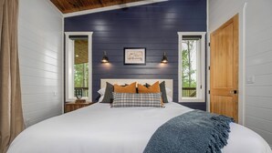 A bedroom with a large bed, a wooden door, and a window with a view of trees.