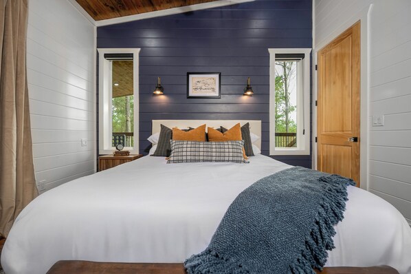 Une chambre avec un grand lit, une porte en bois et une fenêtre donnant sur des arbres.