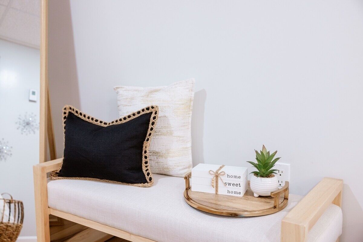 A cozy seating area with a cushioned bench, a decorative pillow, a small potted plant, and a tray with a card and a mug.