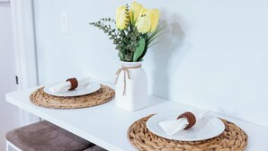 Ett vitt bord med två tallrikar, var och en med en servett och en brun prydnadsföremål, och en vit vas med gula blommor placerad på en vävd bordstablett.
