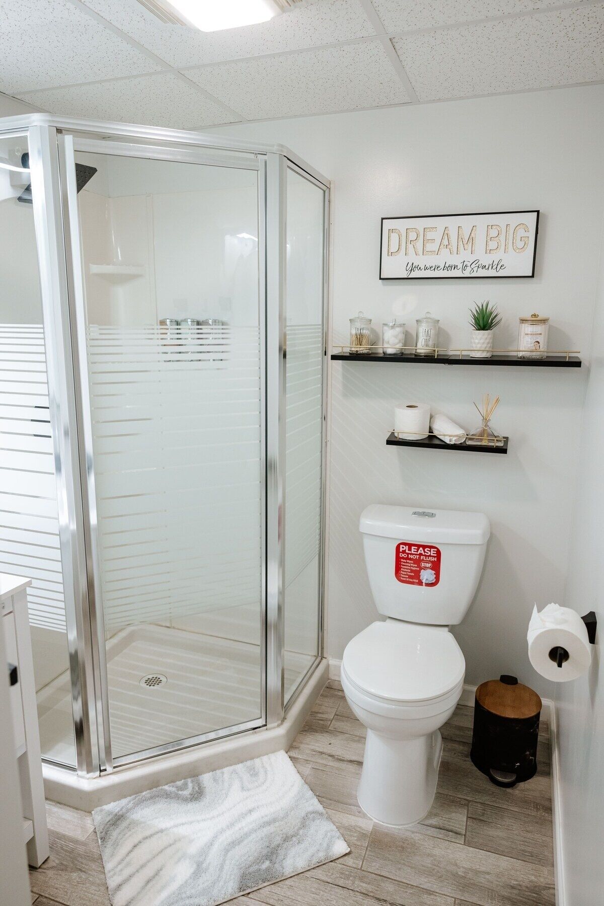 Een badkamer met een douchecabine van glas, een toilet met een bordje 'Niet doorspoelen' en een plank met toiletartikelen.