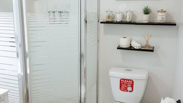 Een badkamer met een douchecabine van glas, een toilet met een bordje 'Niet doorspoelen' en een plank met toiletartikelen.